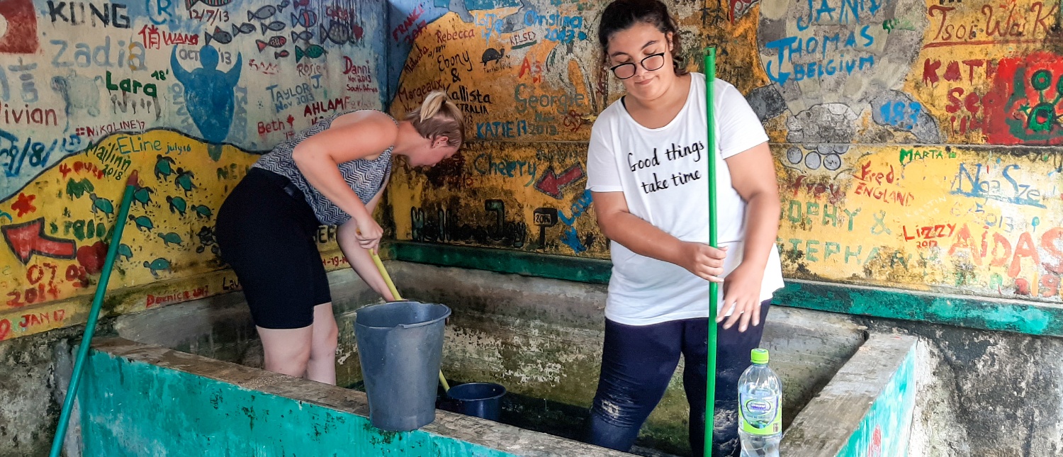 Two women clean a large tank at a turtle conservation center with graffiti walls in Ambalangoda, Sri Lanka.
